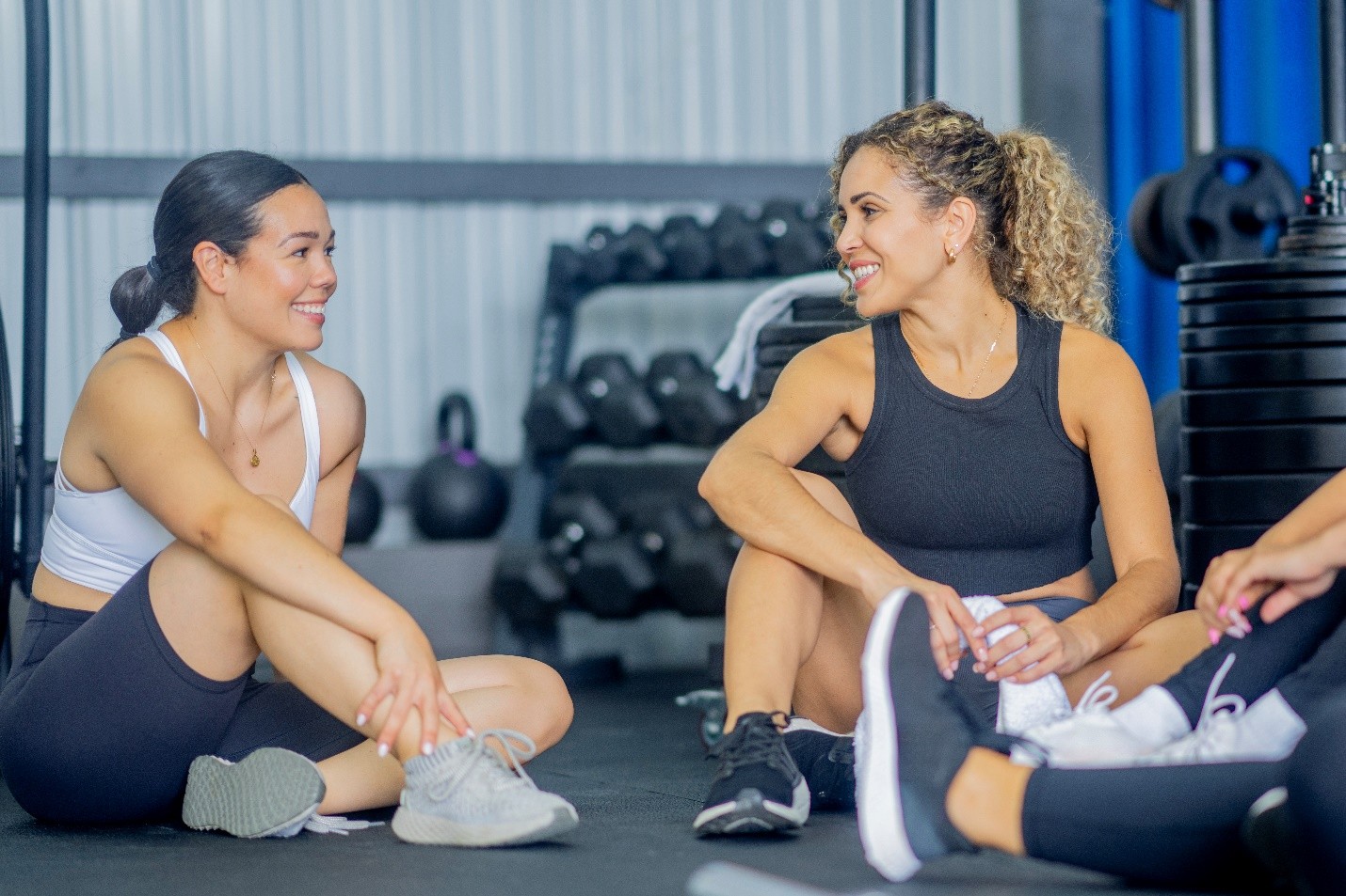 Two woman sitting down post-workout in a room filled with weights looking happy and strong.